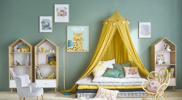 Chambre de fille tendance avec lit au sol, ciel de lit jaune, coussins animaux et étagères en forme de maison.