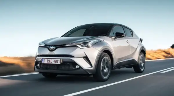 Srebrna Toyota C-HR 2023 pędzi po pustej drodze, z zachodzącym słońcem w tle.