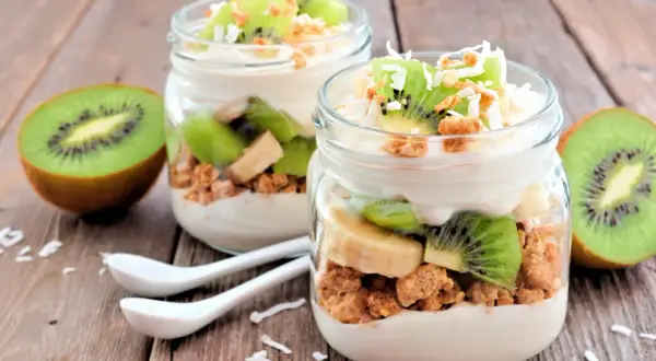 Två glas med yoghurt, granola, kiwi och banan. Perfekt mellanmål att ta med.