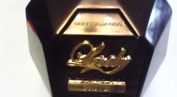 Złote logo "Lady" na ciemnym flakonie perfum, z napisem "Prive" poniżej. Elegancki dodatek dla każdej kobiety.