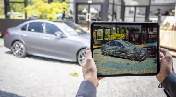 Persona usa una tablet para ver un modelo 3D de un Mercedes, mostrando los componentes internos para entender los mantenimientos.