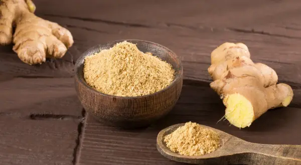 Ingwerpulver verwendung: frischer Ingwer und eine Schale mit feinem Ingwerpulver auf dunklem Holz.