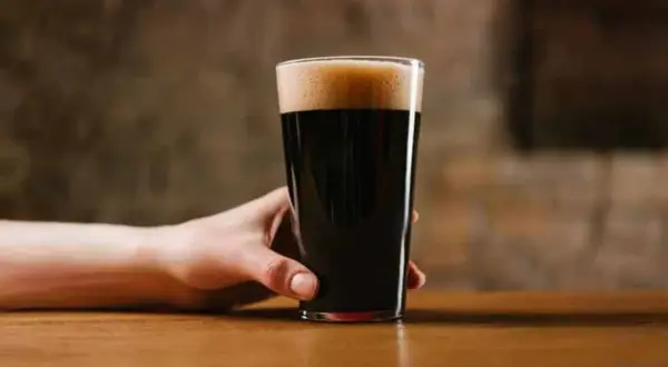 Ręka trzymająca szklankę ciemnego piwa porter. Czy piwo porter jest zdrowe? To pytanie zadaje sobie wielu miłośników tego trunku.