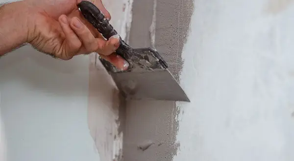 Mano che stende premiscelato per chiudere tracce su un muro con una spatola.