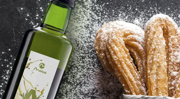 Botella de aceite de oliva junto a churros espolvoreados con azúcar glas.