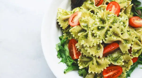 Un piatto invitante di pasta fredda al pesto, con farfalle condite e pomodorini freschi, guarnito con insalata verde.