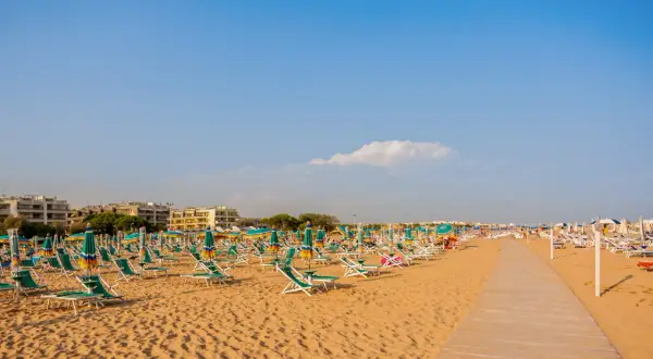 Szeroka, piaszczysta plaża w Bibione z rzędami leżaków i parasoli pod błękitnym niebem.