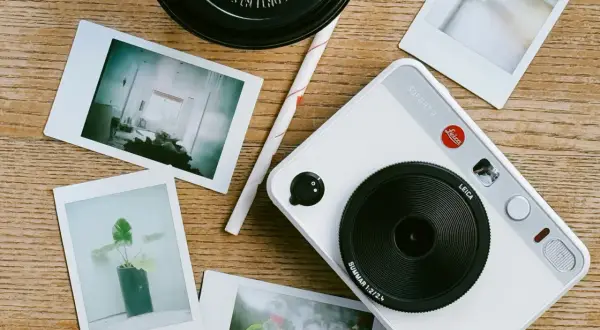 A white Leica Sofort 2 camera with instant photos scattered around. This setup inspires ideas on how to organize photos into folders.