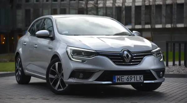 Srebrny Renault Megane 4 z nowoczesnymi żarówkami z przodu, zaparkowany przed budynkiem.