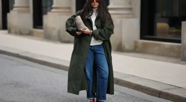 Stylische Frau in dunkelgrünem Mantel und Barrel Jeans, die sie lässig kombiniert. Sie trägt eine weiße Rollkragenpullover und auffällige Schuhe.