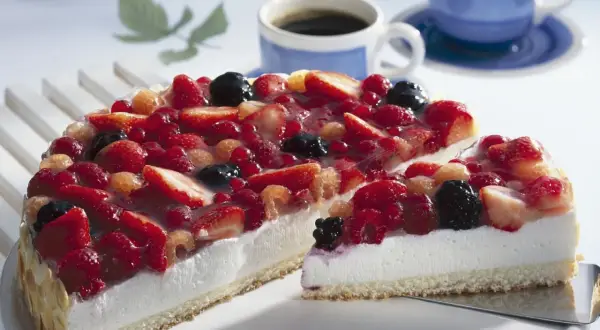 Eine einfache Torte mit frischen Beeren, bedeckt mit Tortenguss. Daneben zwei Tassen Kaffee.