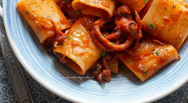 Paccheri con sugo di calamari, un piatto di mare saporito e colorato, con tentacoli che spuntano dalla pasta.