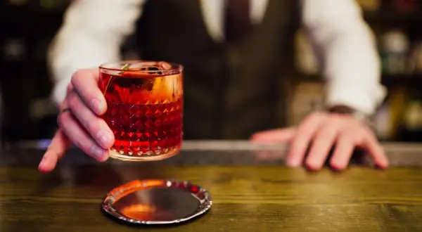 Ein Barkeeper reicht einen roten Cocktail mit Eis und Garnitur. Perfekt, um cocktail mixen lernen.