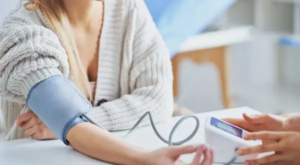 Kobieta z mankietem ciśnieniomierza na ramieniu, zastanawia się, czy ashwagandha obniża ciśnienie.