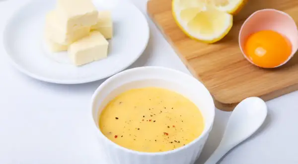 Tazón con salsa holandesa, mantequilla en cubos, limón y yema de huevo. Ingredientes para una deliciosa salsa.