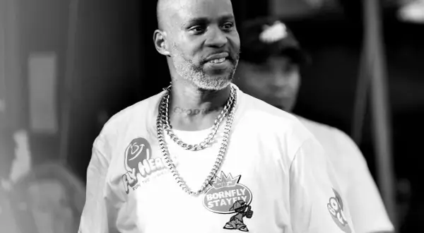 DMX w białej koszulce z łańcuchem na szyi, z tatuażem "EXODUS" na karku, uśmiecha się podczas występu.