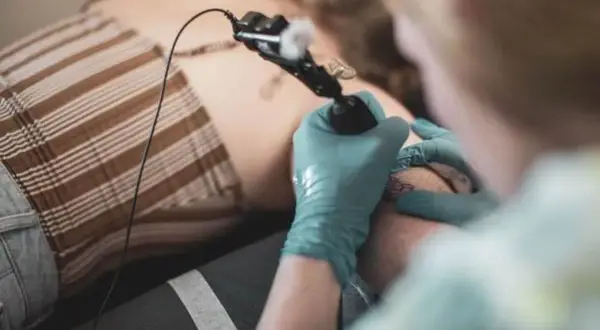 Tatuador con guantes azules haciendo un tatuaje de puñal en la pierna de una persona.