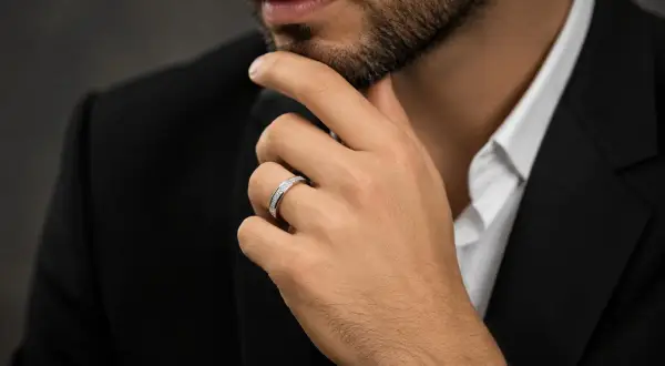 Un hombre con traje negro y camisa blanca luce un elegante anillo bulgari oro blanco y amarillo, adornado con diamantes.