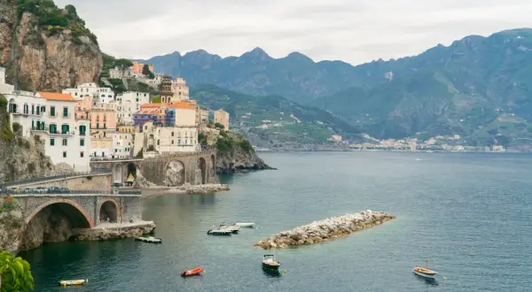 Malownicze miasteczko na klifie wzdłuż wybrzeża Amalfi, z łodziami na lazurowej wodzie i górami w tle.