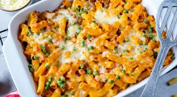Herzhaftes Rigatoni al Forno mit Erbsen und geschmolzenem Käse in einer Auflaufform, bereit zum Servieren.