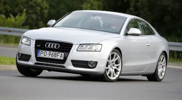 Srebrne Audi A5 z 2006 roku na drodze, z widocznym kierowcą.