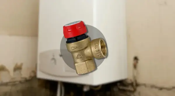 Gros plan sur un montage soupape de sécurité chaudière en laiton avec un capuchon rouge, installé sur une chaudière blanche.