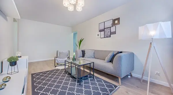 Nowoczesne lampy sufitowe do niskich pomieszczeń rozświetlają salon z szarą kanapą i geometrycznym dywanem.
