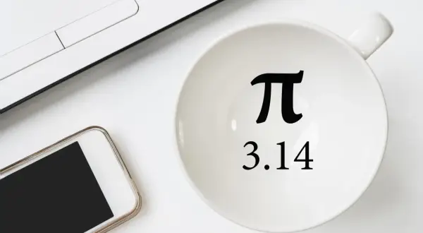 Biały kubek z symbolem π i liczbą 3.14, obok smartfon i fragment laptopa.