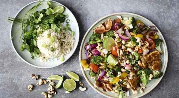 Två tallrikar med mat: en med ris, koriander och lime, den andra med kyckling, grönsaker och cashewnötter. Perfekt för nyttiga recept!