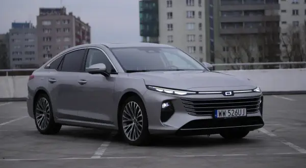 Srebrny Bestune B70 z nowoczesnymi światłami LED zaparkowany na betonowym placu, w tle budynki mieszkalne.