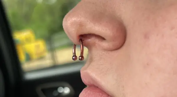 Metalowy kolczyk w nosie, w tym w przegrodzie nosowej (septum), z dwoma kulkami. Wygląda na to, że jest to idealne miejsce na taki dodatek, czyli sweet spot septum.