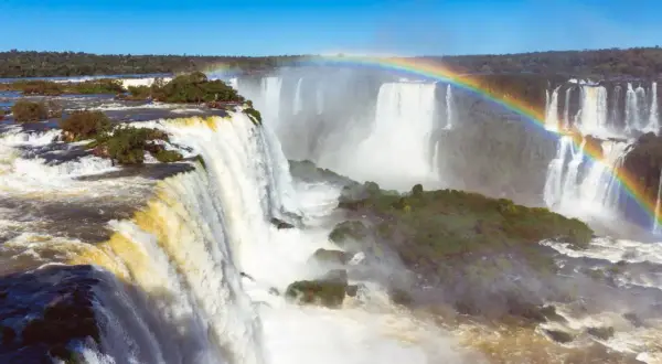 Potężny wodospad Iguazu, z tęczą unoszącą się nad mgłą wodną, otoczony bujną zielenią.
