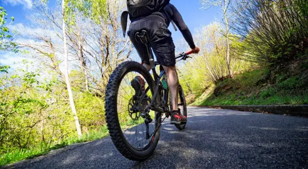 Rowerzysta na ścieżce rowerowej w Białymstoku, otoczony zielenią i błękitnym niebem.