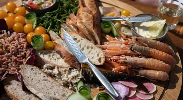 Ein Festmahl mit fisch tapas: Garnelen, Brot, geräucherter Fisch, Tomaten und Gurken auf einem Holzteller.