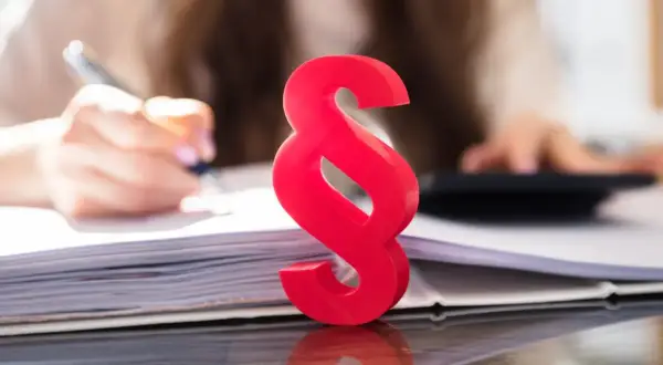 Czerwony symbol paragrafu na tle osoby pracującej z dokumentami i kalkulatorem symbolizuje różne rodzaje wykładni prawa.