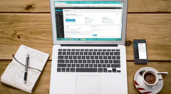 Laptop z panelem WordPress, obok notatnik z planami i telefon. Idealne narzędzia do pracy z XAMPP i WordPress.