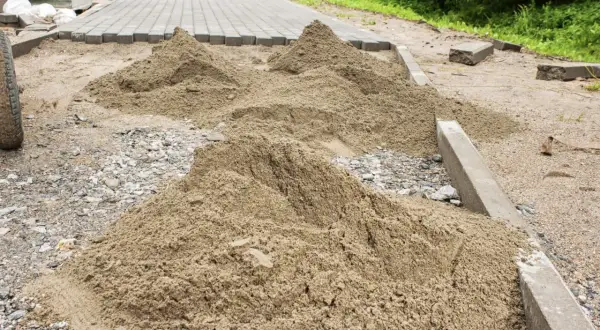 Kopa piasku czeka na ułożenie kostki brukowej. Trudno oszacować, ile piasku na m2 kostki, ale widać, że materiału jest sporo.