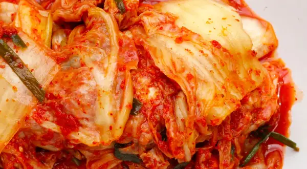 Pikantne, fermentowane warzywa, czyli kimchi co to jest? To danie pełne smaku i zdrowia, z widocznymi liśćmi kapusty i zieloną cebulką.