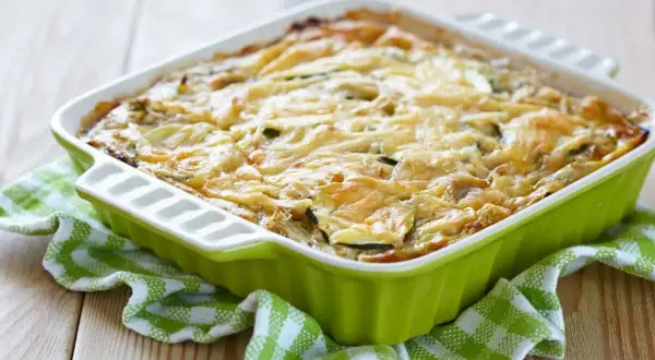 Pastel de calabacín horneado, con queso gratinado y rodajas de calabacín visibles, servido en un recipiente verde sobre un mantel a cuadros.