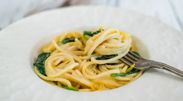 En gaffel lyfter en krämig portion pasta limone med gröna blad och citronskal.