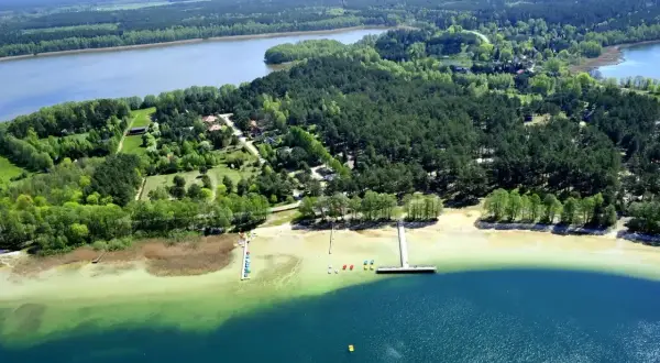 Malownicze jezioro Warchały otoczone lasem, z piaszczystą plażą, pomostami i kolorowymi łódkami.