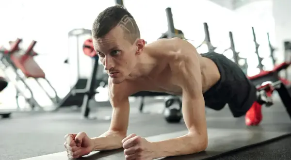 Un homme concentré effectue un gainage dynamique sur un tapis de gym, muscles tendus, dans une salle de sport.