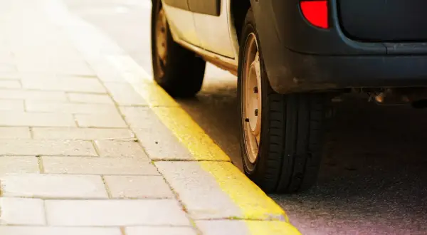Un coche aparcado junto a una acera con marcas viales amarillas. El significado de estas marcas viales amarillas indica prohibición de estacionar.