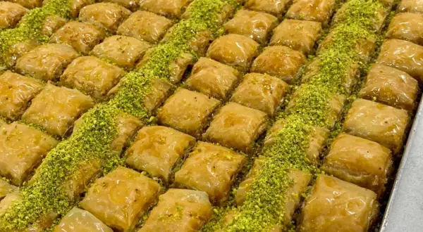 En stor bricka med gyllene, krispiga baklavabitar, generöst strödda med gröna pistagenötter. Perfekt för ett hemlagat baklava recept.