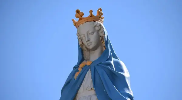 Posąg Matki Boskiej w koronie, symbolizujący czystość i idealizm, na tle błękitnego nieba.