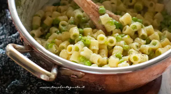 Un primo piatto cremoso di pasta e piselli, mescolata con un cucchiaio di legno in una pentola di rame.
