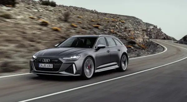Audi RS6 Avant gris en movimiento en una carretera sinuosa, demostrando su velocidad máxima en un paisaje montañoso.