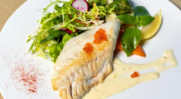 Filet de haddock parfaitement cuit, garni de perles de hareng, servi avec une salade fraîche, des légumes et une sauce crémeuse.