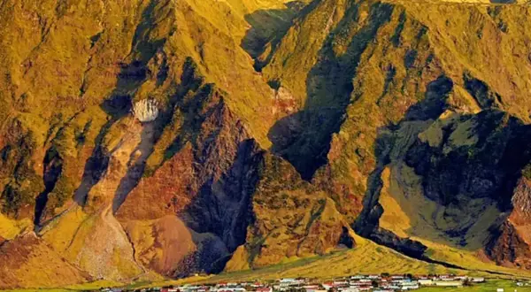 Un pueblo en Tristan de Acuña se asienta al pie de imponentes montañas cubiertas de hierba, bañadas por la luz dorada del atardecer.