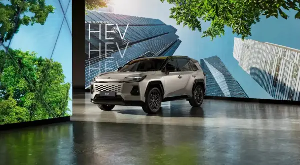 Nowoczesny srebrny Toyota RAV4 HEV prezentowany na tle futurystycznych budynków i zieleni.